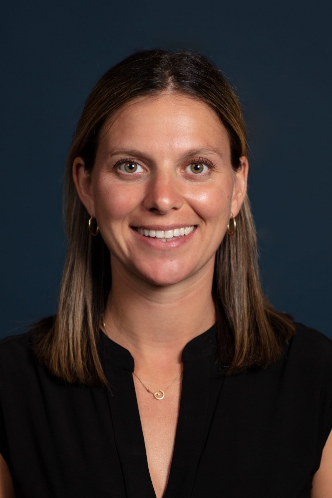 Headshot of Gianna Cacciatore wearing a black v-necked shirt on a dark blue background.